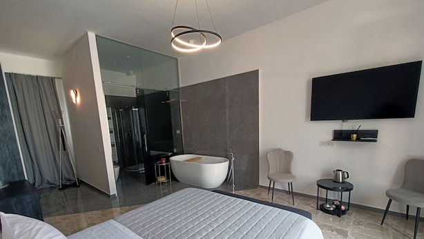 A modern hotel room with a large bed, a walk-in shower, a bathtub, a television, and a coffee table. - La Residenza del Barone (Camerota)