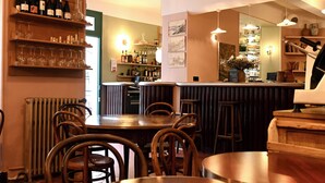 A restaurant interior with wooden tables and chairs, a bar area with shelves of bottles and glasses, and a radiator on the left. - La Résidence Le Provençal (Hyères)