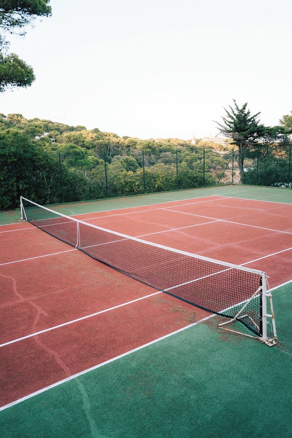 Cancha de tenis con red, rodeada de árboles y una valla.