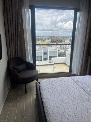 Habitación de hotel con una ventana grande, una cama con colcha estampada, una silla y vistas a la ciudad.