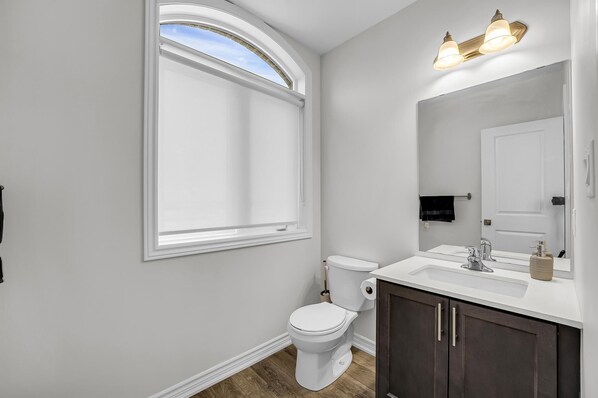 Une salle de bain avec des toilettes blanches, un lavabo avec un miroir et une fenêtre donnant sur le ciel.