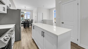 Une cuisine moderne avec des meubles blancs, un îlot central et un coin repas comprenant une table et des chaises.