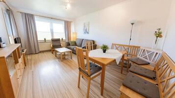 Ein geräumiger Wohnbereich mit Holzboden, einer Couch, einem Esstisch mit Stühlen und einer Lampe.