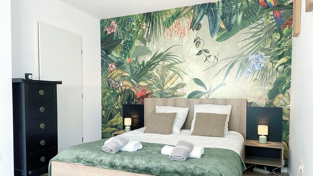 A bedroom with a bed, two bedside tables, a nightstand, a dresser, and a large tropical-themed mural on the wall. - 3 bedroom townhouse with garden, terrace and private parking (Reims)
