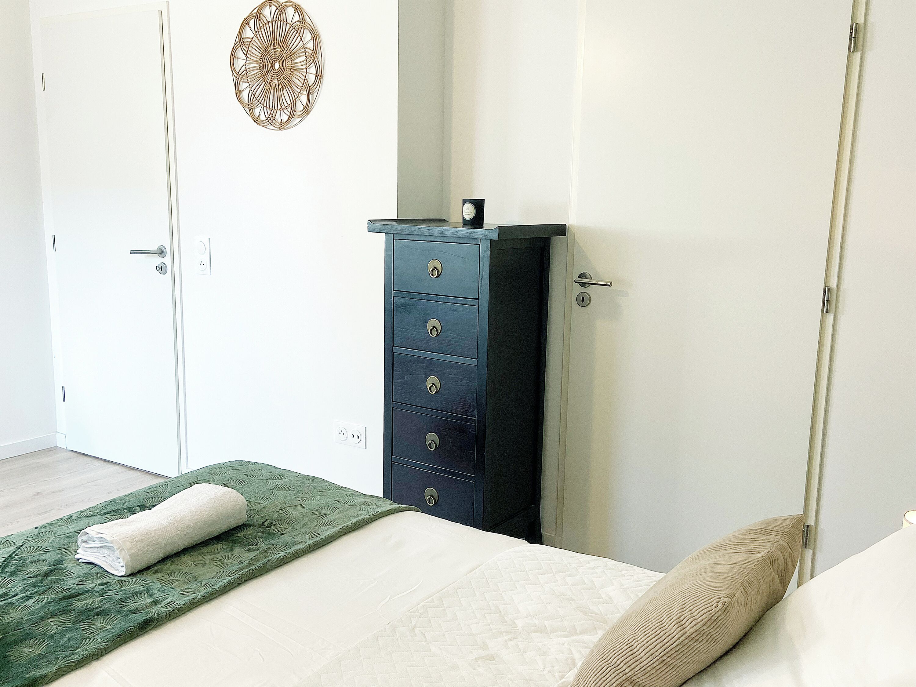 Un dormitorio con una cama, una toalla verde, un aparador azul oscuro y una puerta blanca.