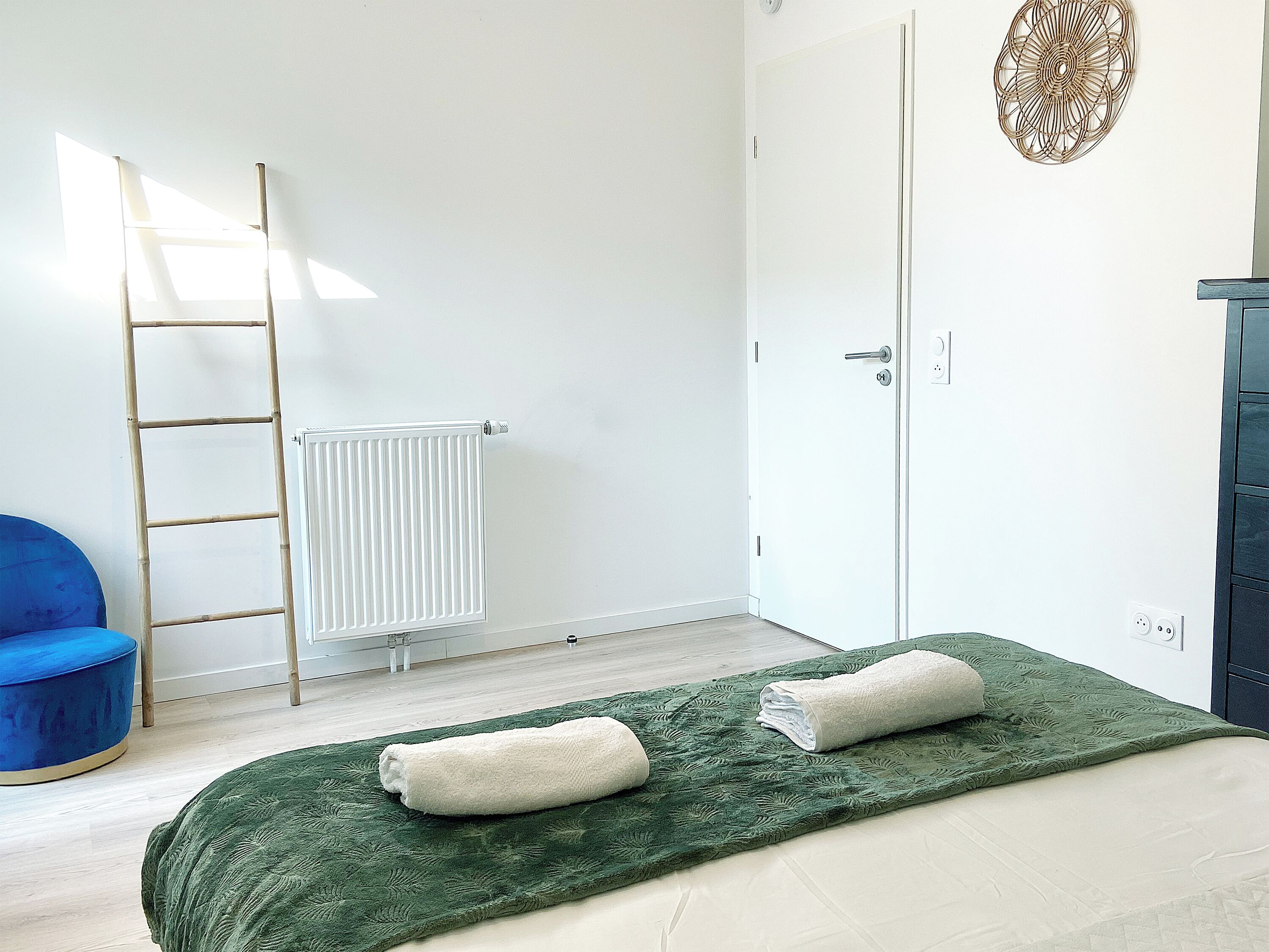 A bedroom with a bed, a ladder, a radiator, a door, and a blue chair.