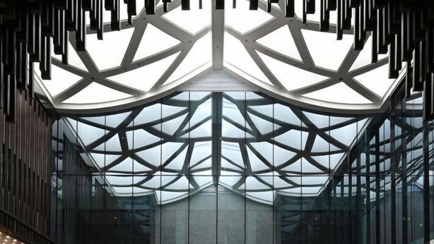 A spacious lobby with a high ceiling, geometric glass panels, and a central circular light fixture.