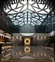 A spacious lobby with a high ceiling, geometric glass panels, and a central circular light fixture.