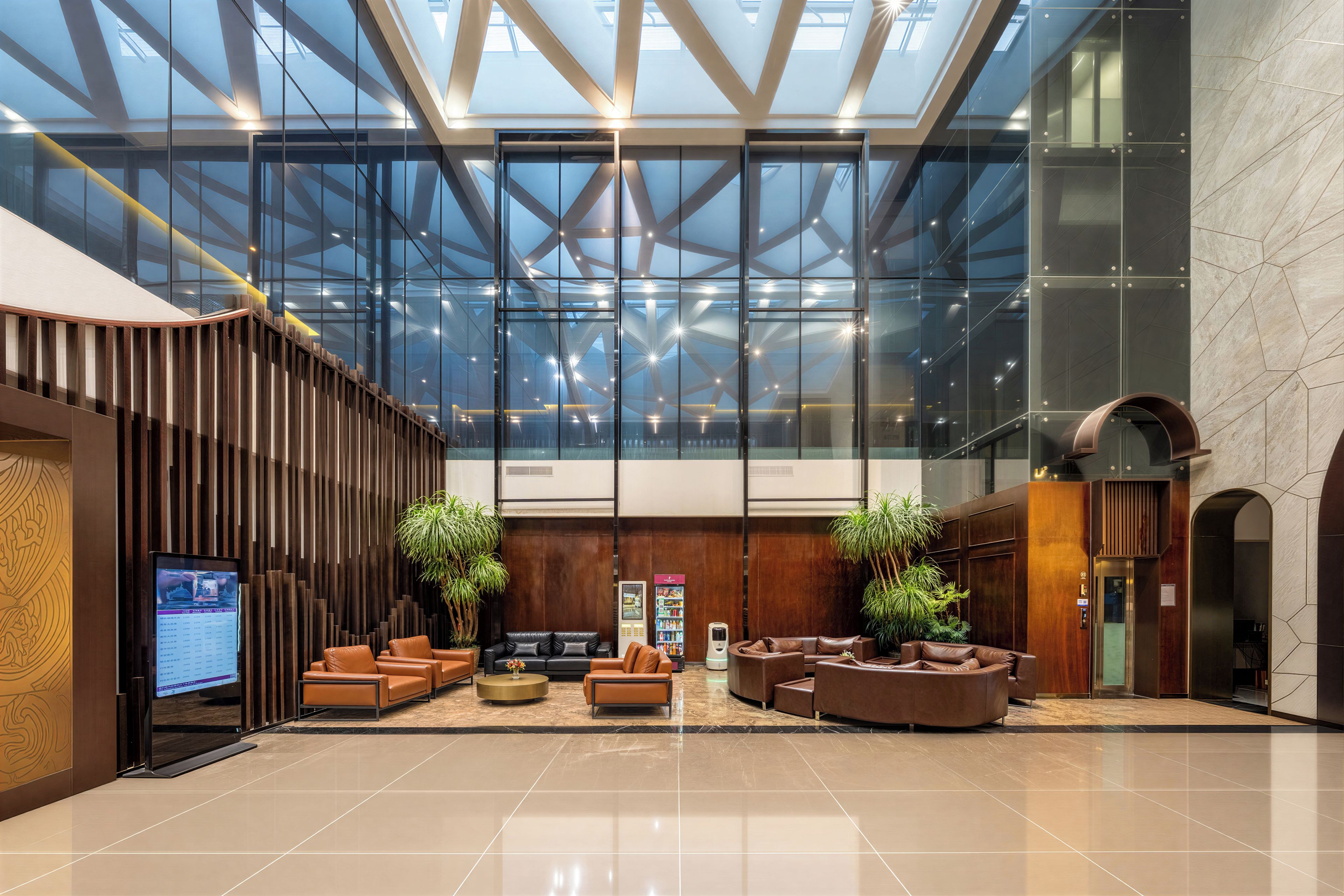 A modern lobby with a high ceiling, glass walls, and a central seating area with leather sofas.