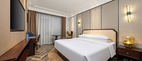 A hotel room with a large bed, a desk, a chair, a TV, and a bedside table with a lamp.