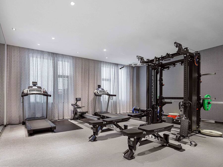 A modern hotel gym with treadmills, weight machines, and a squat rack.