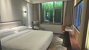 A modern hotel room with a large bed, a desk, a chair, and a TV.