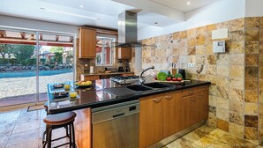 Une cuisine moderne dotée d’un îlot central, d’appareils électroménagers en acier inoxydable, de meubles en bois et d’un pare-feu en pierre.