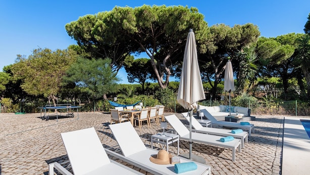 Un espace aménagé au bord de la piscine, avec des chaises longues blanches, une table et des parasols.