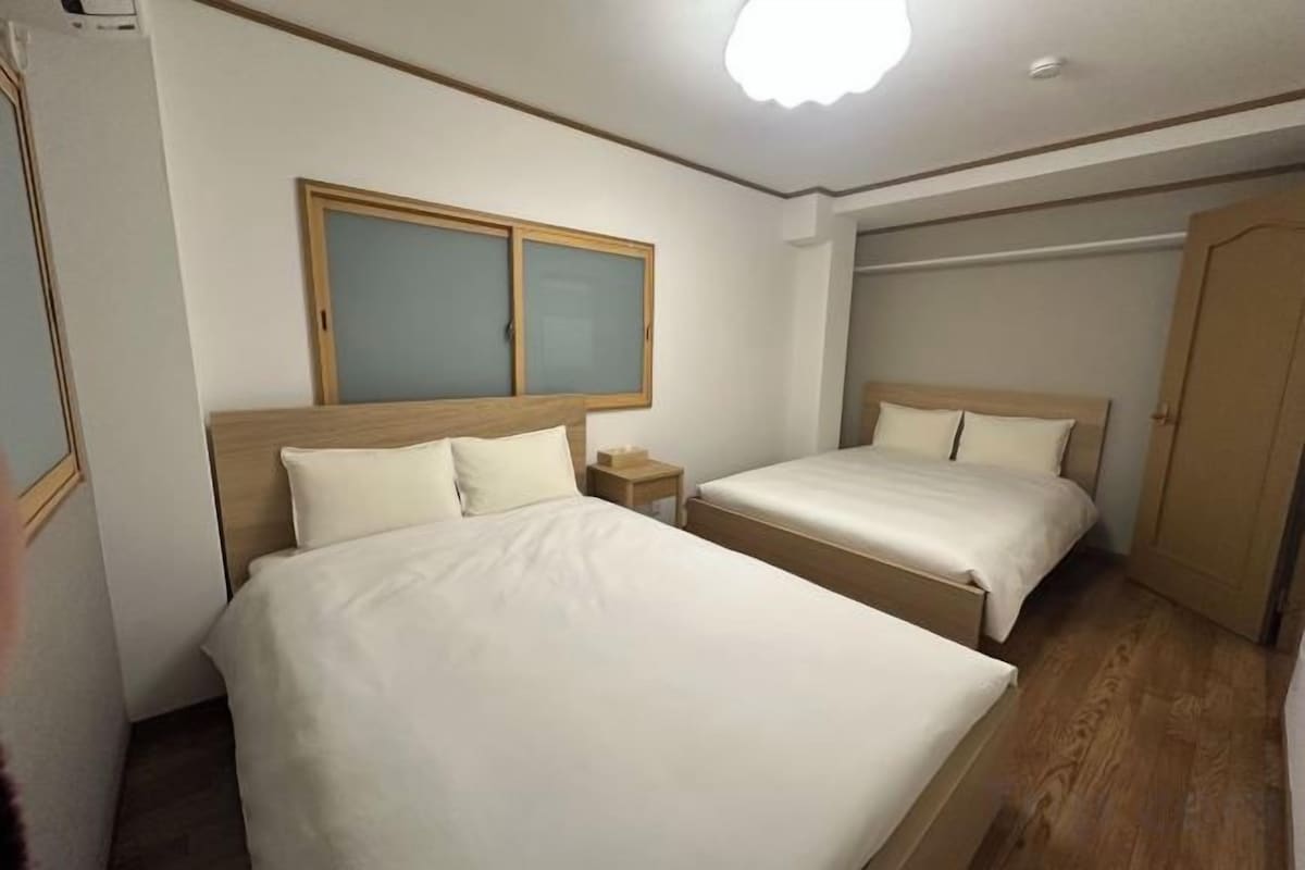 Una habitación de hotel con dos camas, cabecero de madera, mesita de noche y armario.