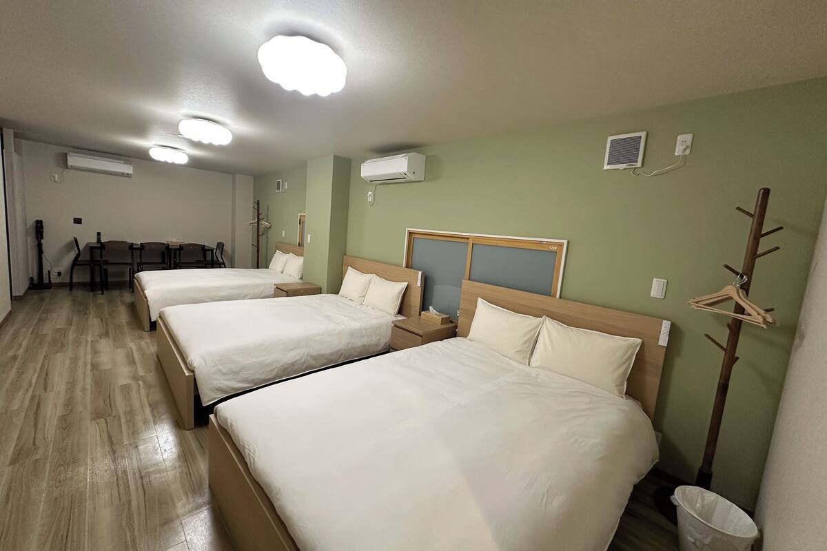 A hotel room with three beds, a desk, chairs, and a coat rack.