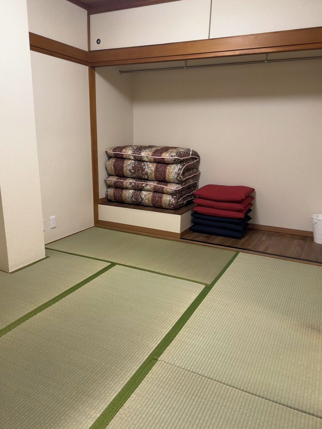 A room with tatami mat flooring, a futon bed, and a small storage area with folded blankets.