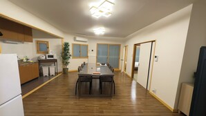 A spacious room with a wooden floor, a central dining table, a kitchen area with cabinets and appliances, and a potted plant. - KAIYOUTATEISHI (Tokyo)