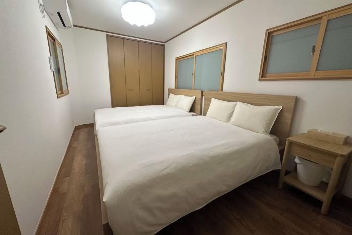 Un dormitorio con dos camas, un armario de madera, una mesita de noche y una ventana con persianas.