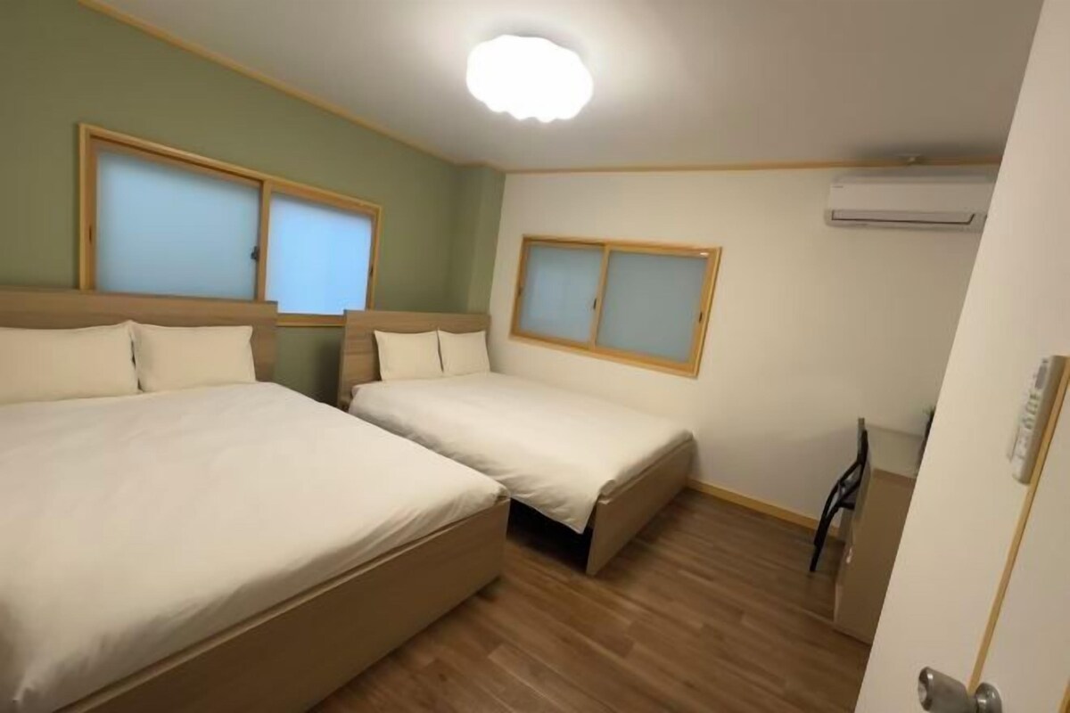 A room with two beds, wooden flooring, and an air conditioning unit on the wall.