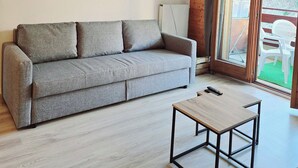 Una sala de estar moderna con un sofá gris, una mesa de centro de madera y un ventanal con vistas a muebles de exterior.