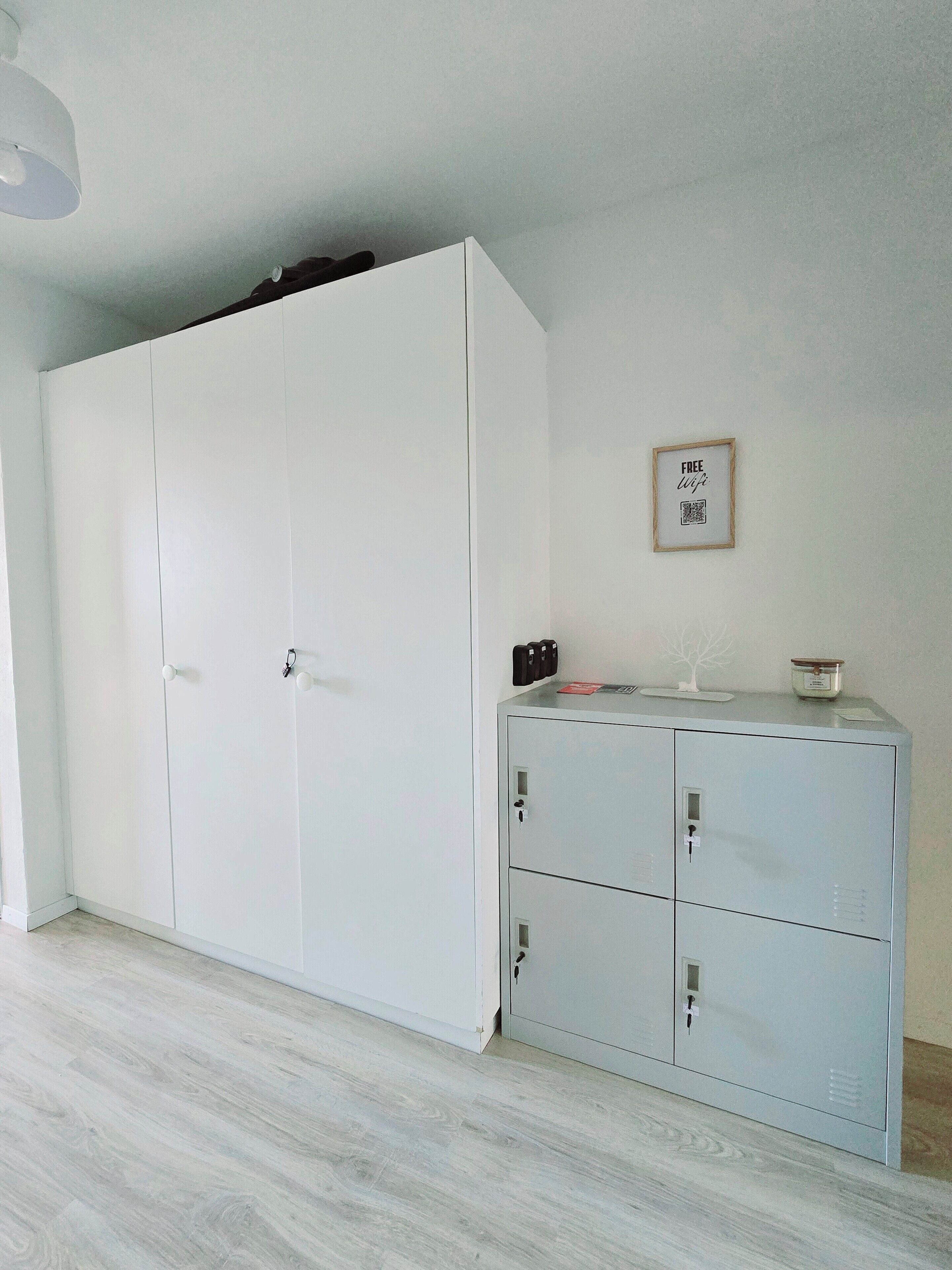 Ein Zimmer mit einem weißen Kleiderschrank, einem Metall-Aktenschrank und einem gerahmten Schild an der Wand.
