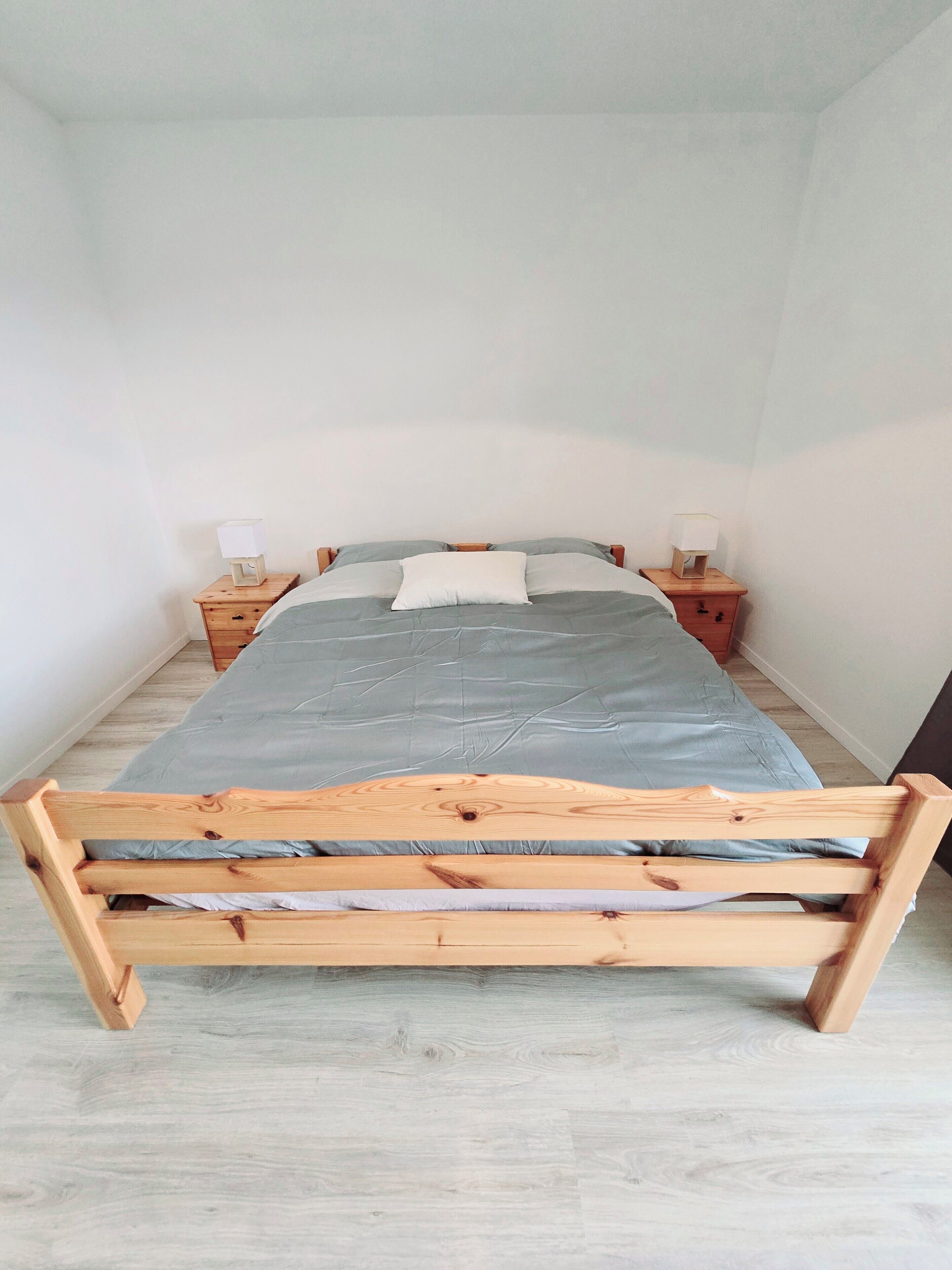 A single bed with a wooden frame, two bedside tables with lamps, and a light-colored wooden floor.