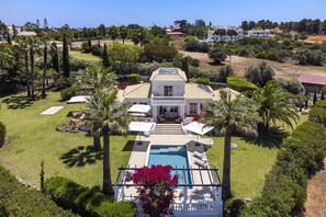 Une grande maison avec une piscine, entourée de palmiers et d’une pelouse bien entretenue.