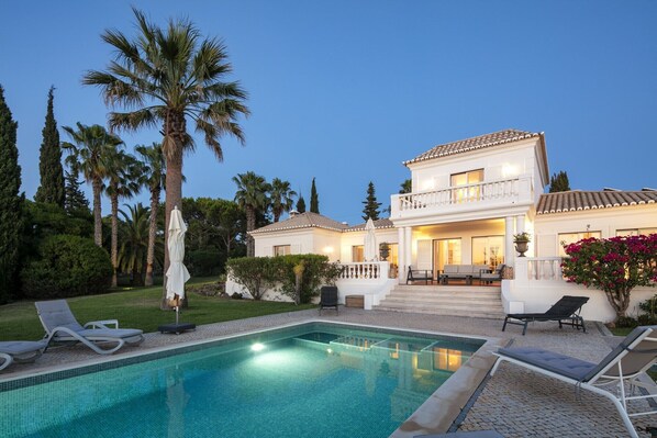 Une maison à deux étages avec une piscine, un espace salon extérieur et des palmiers.