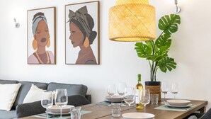 A dining area with a wooden table set for two, two framed artworks on the wall, a hanging woven light fixture, and a potted plant. - Family-Friendly Apartment in Carvoeiro (Carvoeiro)