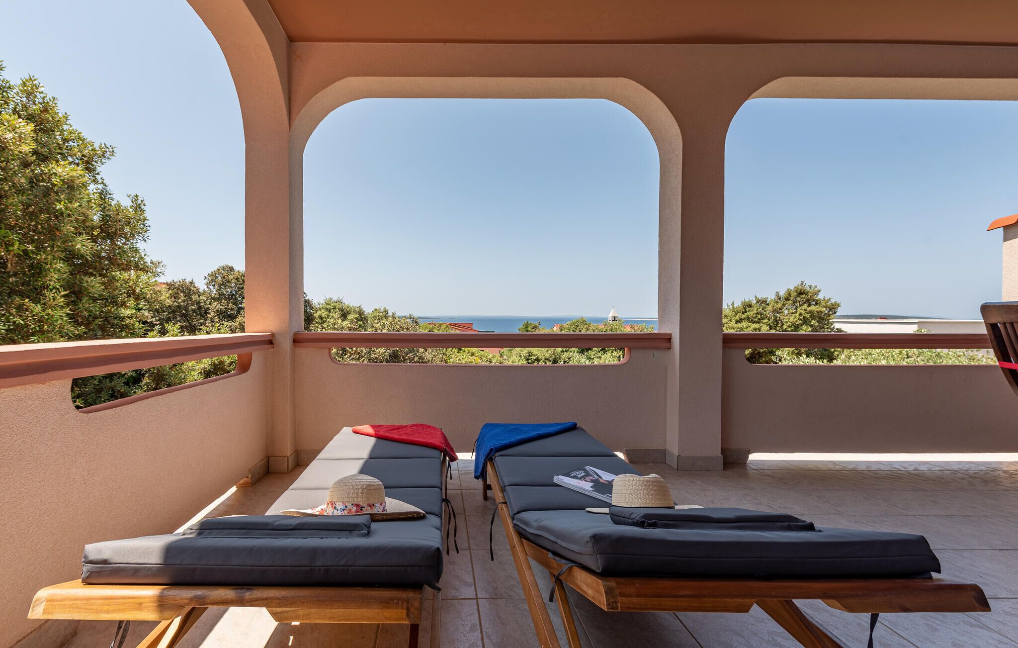 Un balcon avec deux fauteuils de jardin, une table en bois et une vue sur la mer.