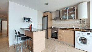 A compact kitchen with a microwave, refrigerator, oven, washing machine, and a small bar area with stools.
