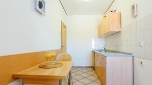 A compact kitchen with a wooden table, two glasses of orange juice, a small wooden chair, and a sink with a faucet.