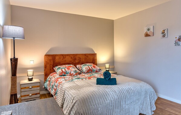 Un dormitorio con una cama, dos lámparas de noche, una mesita de noche, una lámpara y una pared decorada con tres cuadros.