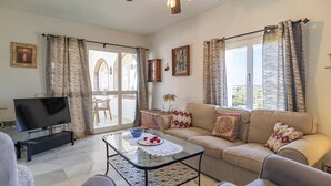A living room with a sofa, a glass coffee table, a TV, and curtains. - Stunning home in Conil de la Frontera (Conil de la Frontera)