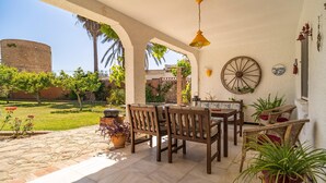 An outdoor patio with a wooden table and chairs, a hanging light fixture, and a large wheel on the wall. - Stunning home in Conil de la Frontera (Conil de la Frontera)