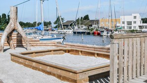 A wooden deck with a concrete platform, surrounded by a wooden fence, overlooking a marina with boats and buildings in the background. - Lovely home in Ebeltoft with sauna (Ebeltoft)