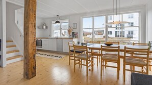 A modern kitchen with white cabinetry, a wooden dining table with chairs, and large windows offering a view of the outside. - Lovely home in Ebeltoft with sauna (Ebeltoft)