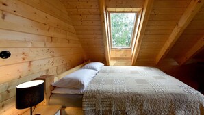 A cozy wooden cabin bedroom with a single bed, a bedside lamp, and a window with a view of trees. - Cozy home in Czaplinek with lake view (Czaplinek)