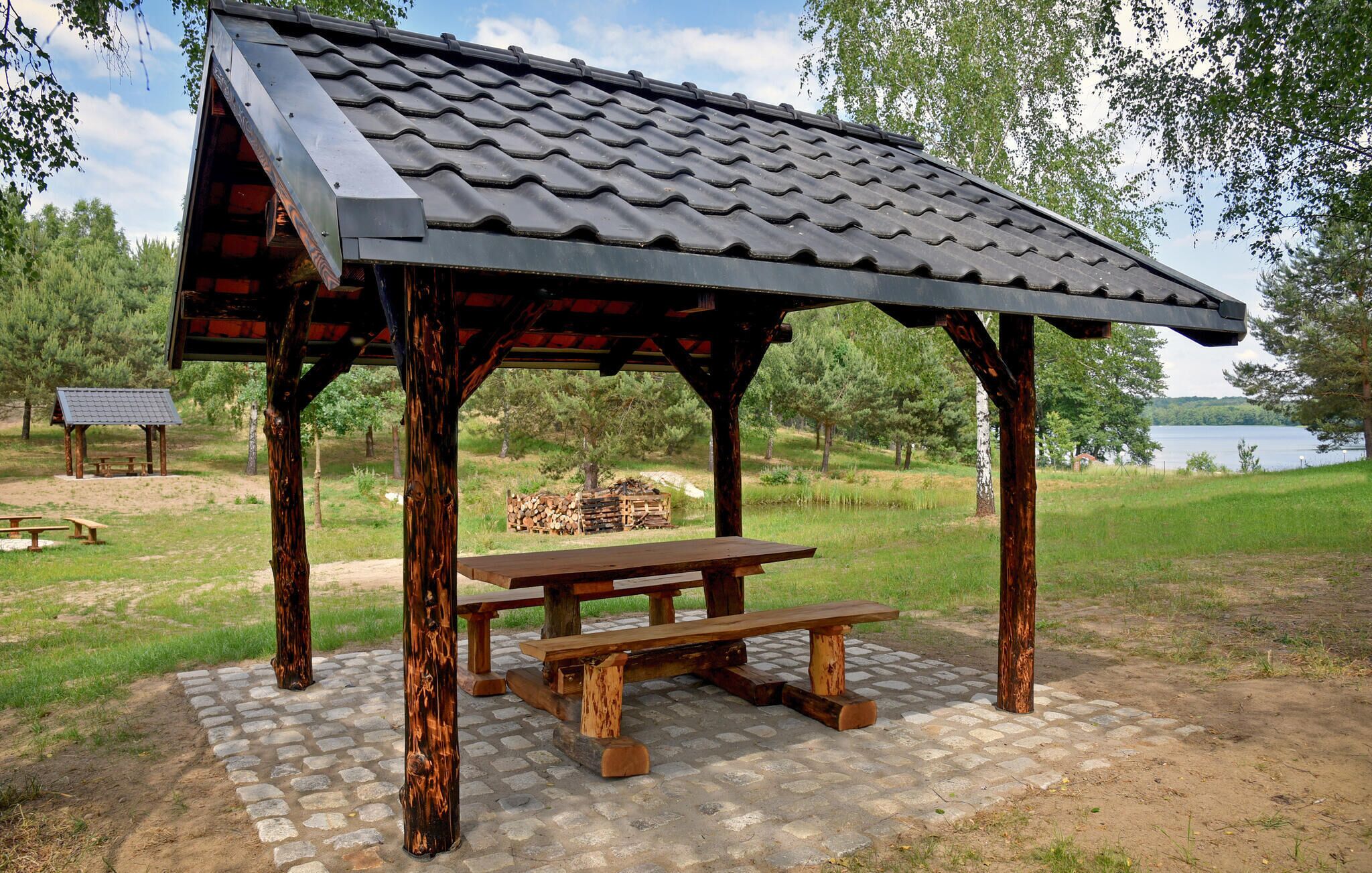 A wooden pavilion with a tiled roof, a picnic table, and a stone-paved area.