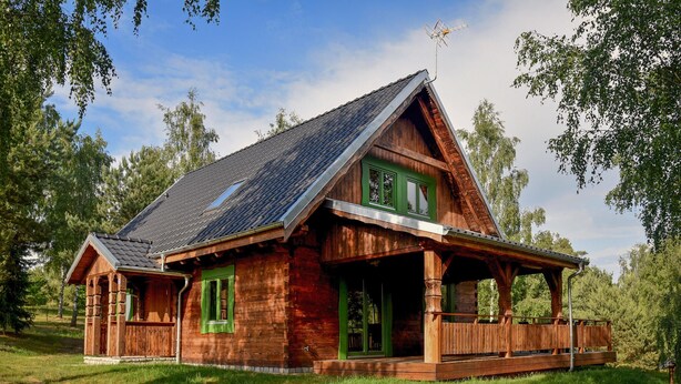 A wooden cabin with a sloped roof, green shutters, and a porch. - Cozy home in Czaplinek with lake view (Czaplinek)