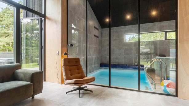 A modern interior with a glass-enclosed pool, a leather chair, and a view of the outdoors.