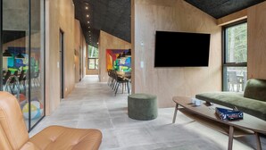 A modern interior with a long corridor leading to a dining area, a flat-screen TV mounted on the wall, and a seating area with a table and ottoman.