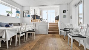Un vaste espace à manger agrémenté d’un escalier en bois menant à un niveau supérieur, de meubles blancs et de grandes fenêtres qui laissent entrer la lumière naturelle.