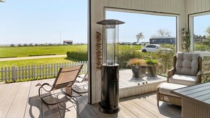 Un balcon donnant sur un champ verdoyant et des voitures garées, avec une chaise en osier, une table et un radiateur.