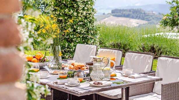 Mobiliario de comedor al aire libre con sillas de mimbre y una mesa dispuesta para el desayuno.