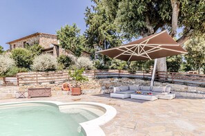 Ein Poolbereich mit Steinböden, einer Lounge-Ecke mit Kissen und einem großen Sonnenschirm.