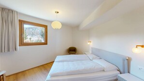 A bedroom with a bed, a chair, a window with a view, and a pendant light.