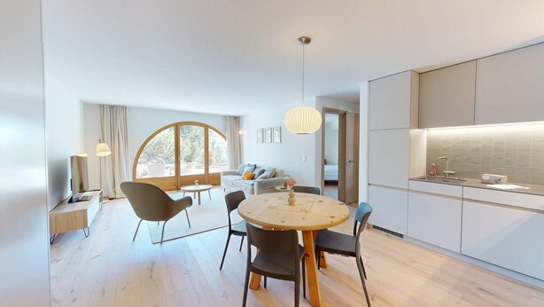 A modern kitchen with a dining area, large windows, and a view of the outdoors.