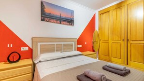A hotel room with a bed, a wooden nightstand, a painting of a sunset, and a wooden wardrobe. - Diana Apartment (Teulada)
